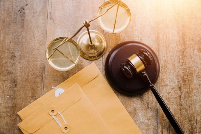 An image showing a judge's gavel, a pair of scales, and two brown legal envelopes on a wooden surface