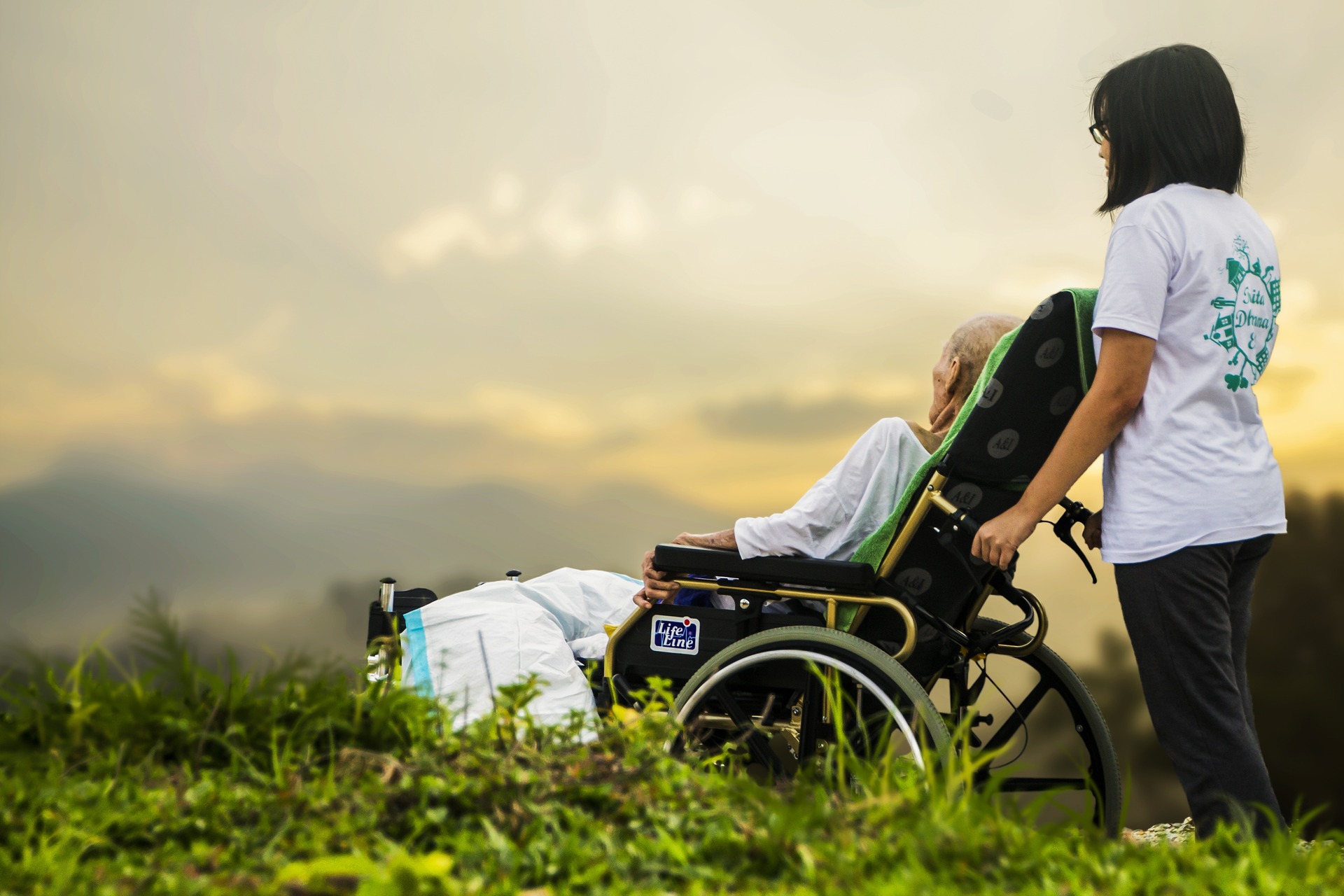 Elderly person in wheelchair being pushed by woman outside