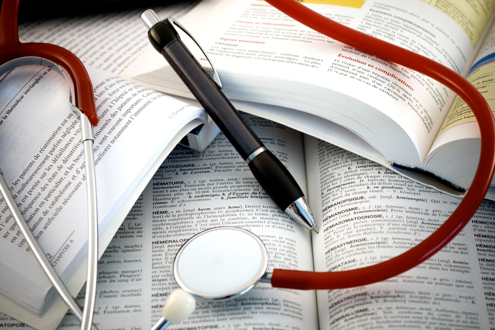 A close-up of medical textbooks open to various pages, with a stethoscope draped across the books and a pen resting on top. 