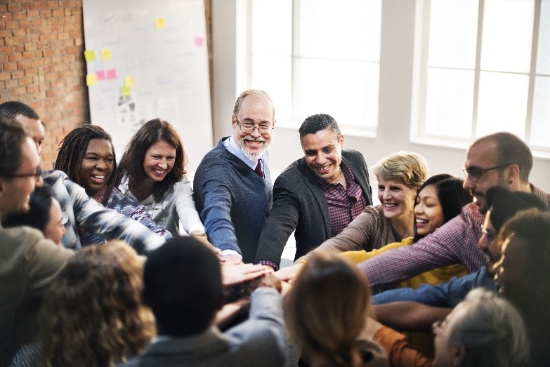 A diverse group of professionals standing in a circle with their hands stacked together in the center, smiling