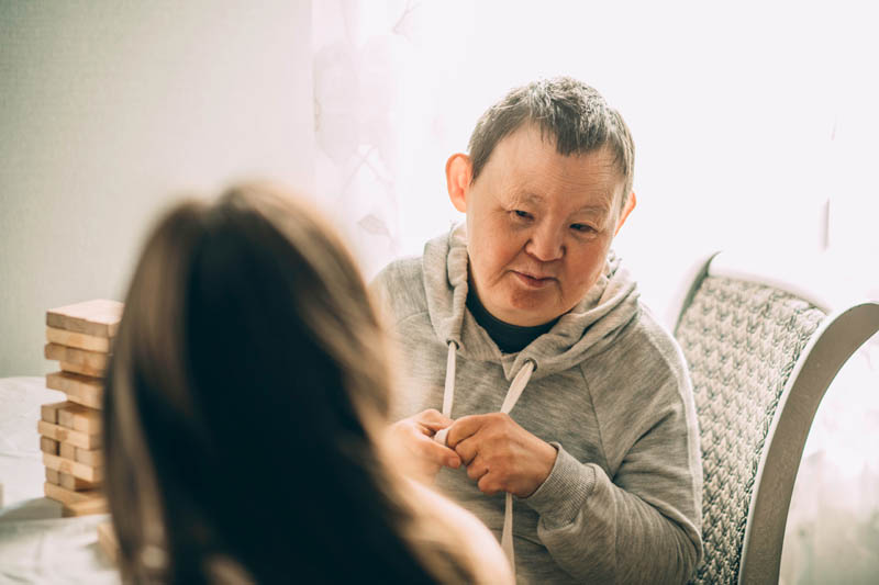 An elderly woman with Down syndrome, accompanied by an assistant who supports her