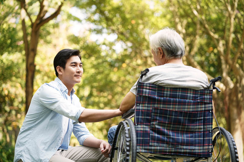 Young man talking to wheelchair bound elderly man