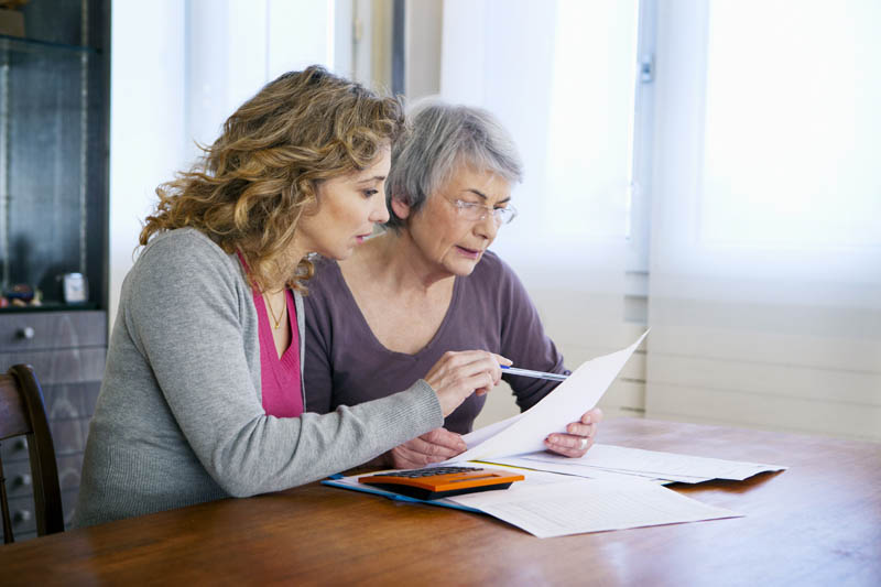 A middle-aged woman and an elderly woman sitting at a table, reviewing documents together