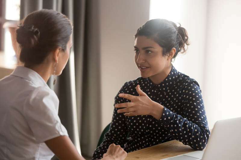 Two women engaged in a conversation at a table, with one woman gesturing while speaking and the other attentively listening