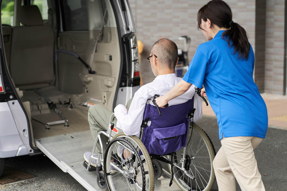 A caregiver assisting a person in a wheelchair, guiding them up a ramp into a specially equipped van.