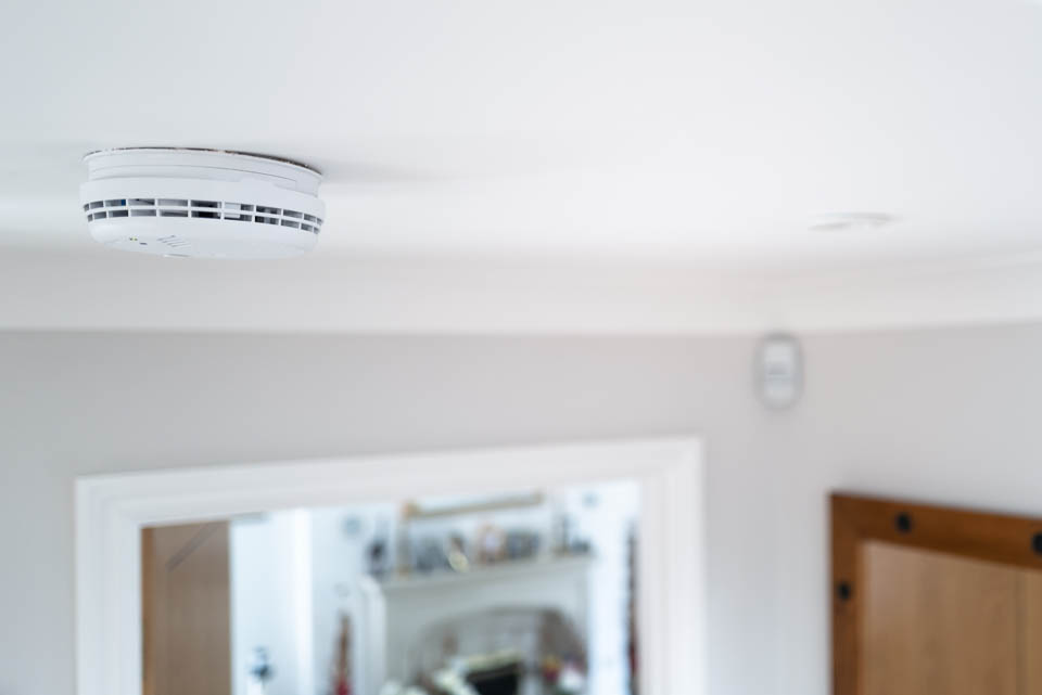 A white smoke alarm is mounted on a white ceiling inside a home