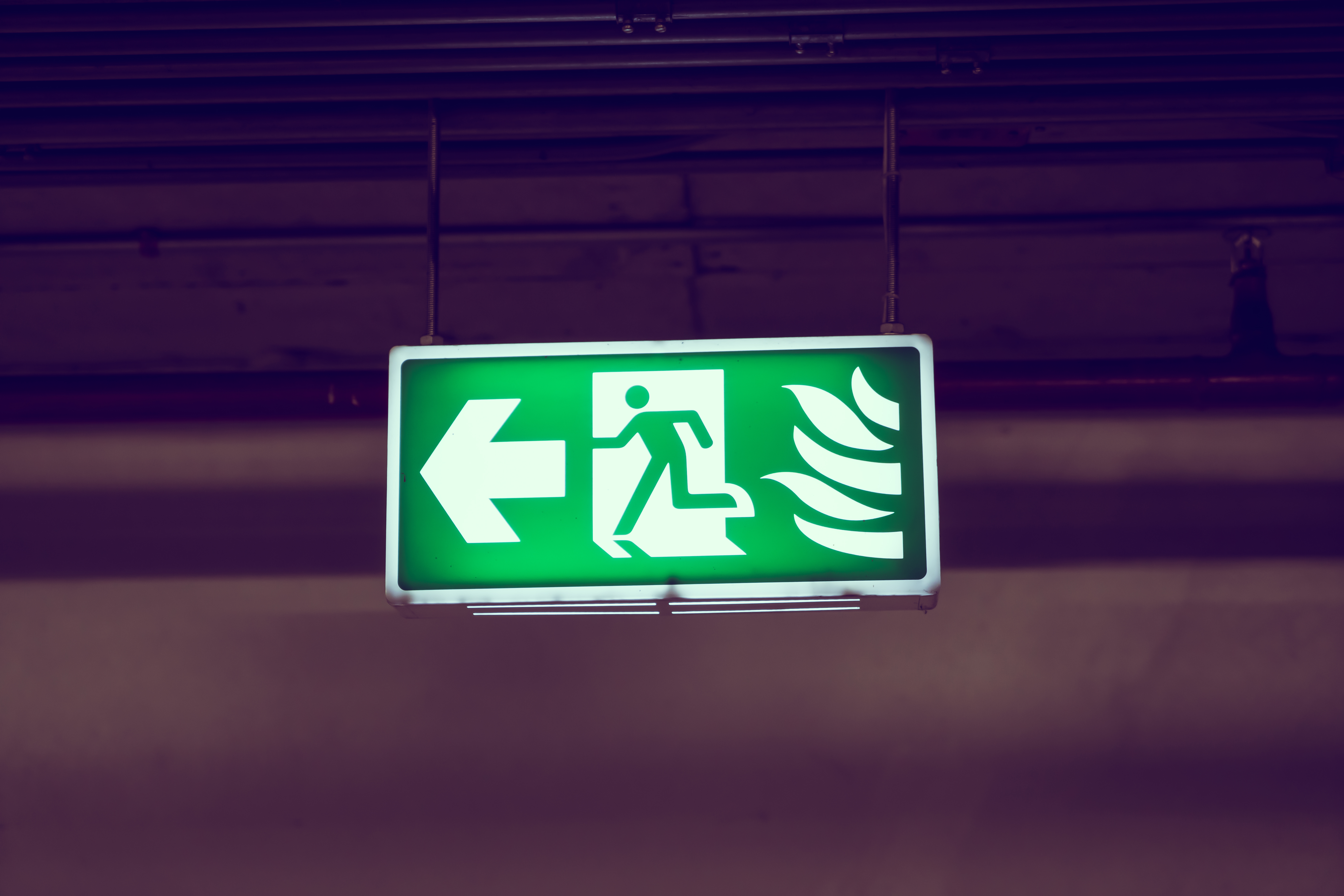 A green sign with a running person and an arrow pointing left, indicating an emergency exit path