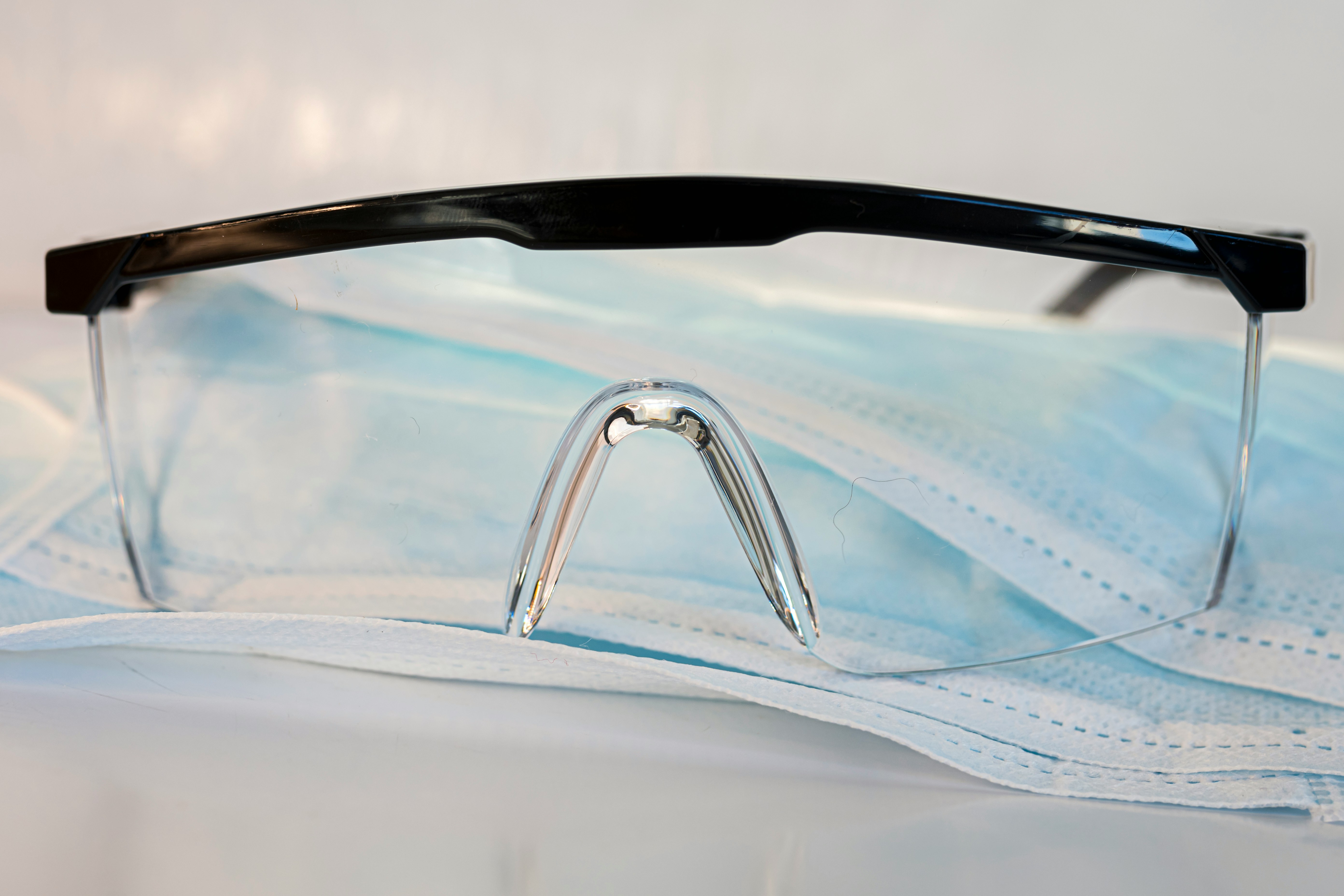 Close-up of transparent protective glasses placed on a blue disposable face mask