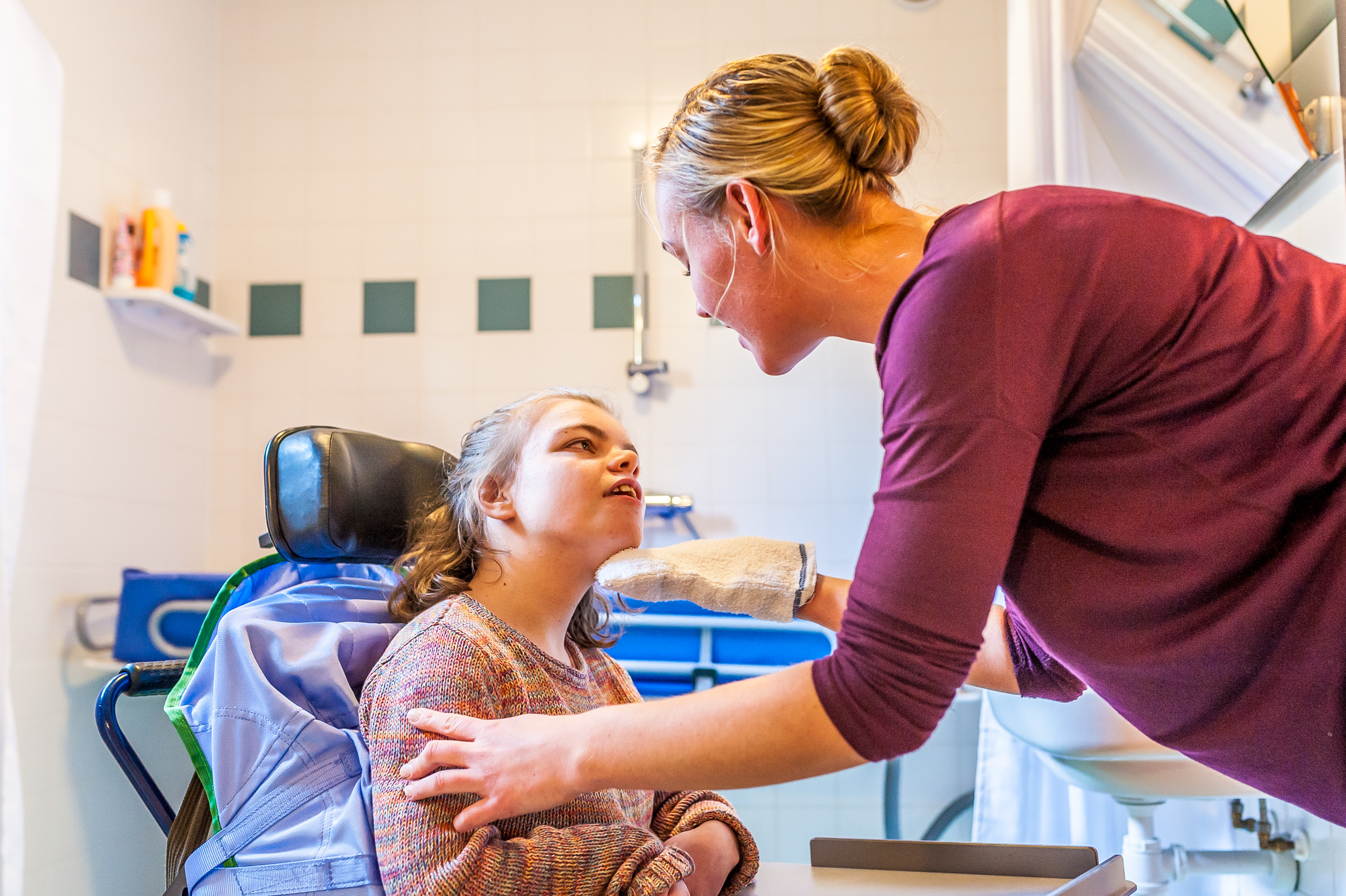 A support worker assists a young disabled girl clean her face.