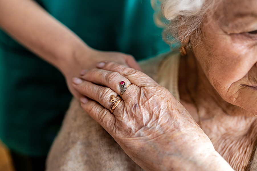 Elderly lady holding another person's hand that is on her shoulder